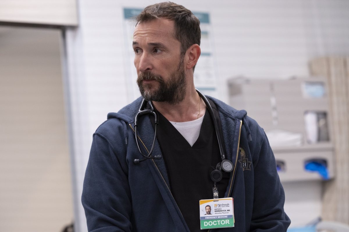 Actor Noah Wyle as Dr. Michael "Robby" Robinavitch in the Max original medical drama series The Pitt, wearing a navy hoodie and stethoscope in a hospital setting.